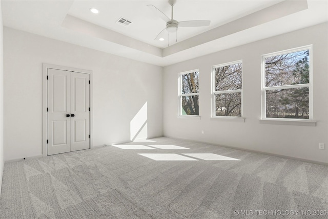 spare room featuring a tray ceiling, carpet, and visible vents