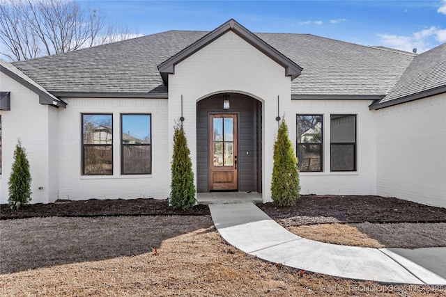 entrance to property featuring brick siding and a shingled roof