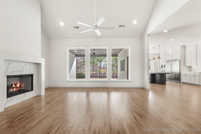 unfurnished living room featuring visible vents, light wood-style floors, ceiling fan, and a premium fireplace