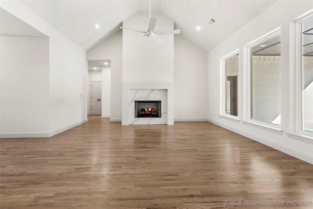 unfurnished living room featuring a high end fireplace, visible vents, light wood-type flooring, and ceiling fan