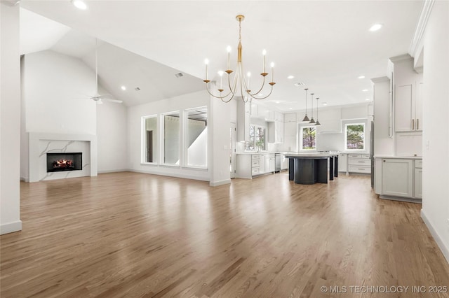 unfurnished living room featuring light wood-type flooring, lofted ceiling, a high end fireplace, and ceiling fan with notable chandelier