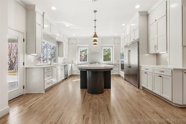 kitchen with backsplash, a center island, stainless steel appliances, light wood finished floors, and light countertops