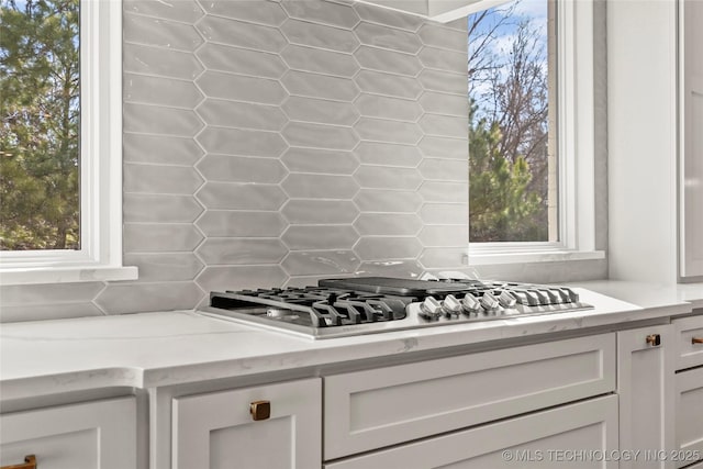 kitchen featuring light stone counters, decorative backsplash, stainless steel gas stovetop, white cabinets, and log walls