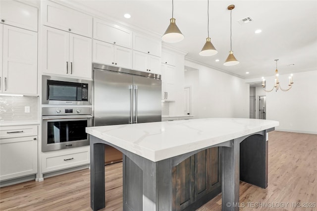 kitchen with visible vents, a kitchen island, ornamental molding, white cabinets, and built in appliances