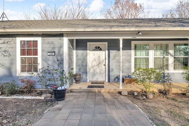 view of exterior entry featuring covered porch and a shingled roof