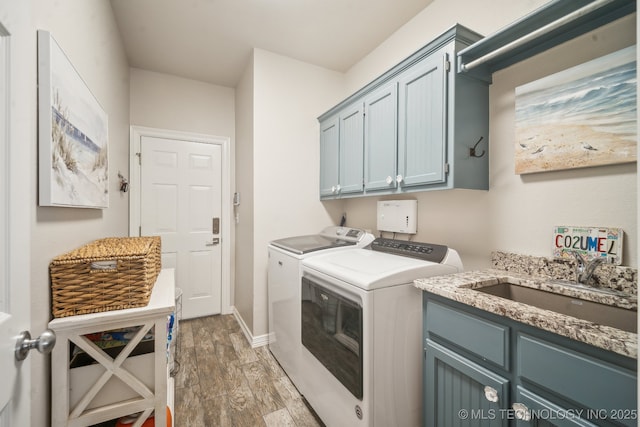 clothes washing area featuring wood finished floors, a sink, independent washer and dryer, baseboards, and cabinet space