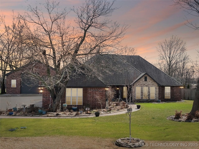 view of front facade featuring roof with shingles, a lawn, and brick siding