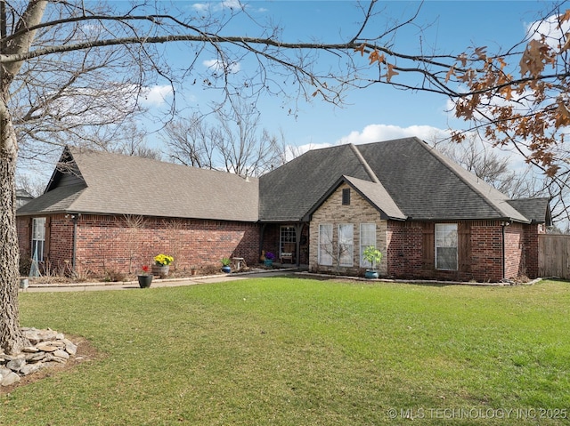 view of front facade with a shingled roof, a front lawn, and brick siding