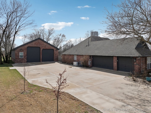 view of property exterior featuring a chimney, a shingled roof, an outdoor structure, a detached garage, and brick siding