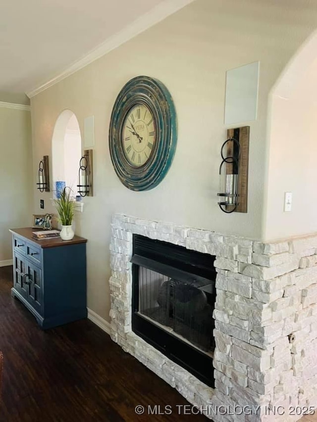 interior details with baseboards, ornamental molding, wood finished floors, and a stone fireplace