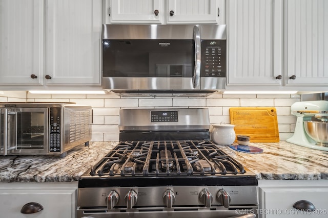 kitchen with a toaster, tasteful backsplash, white cabinetry, light stone counters, and appliances with stainless steel finishes