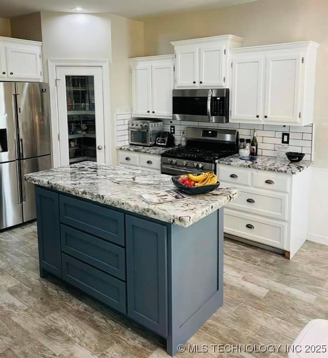 kitchen with stainless steel appliances, light stone countertops, white cabinets, and tasteful backsplash