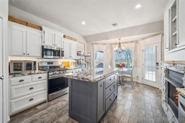 kitchen with stainless steel appliances, visible vents, gray cabinetry, a kitchen island, and a stone fireplace