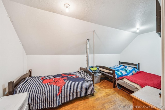 bedroom featuring a textured ceiling, vaulted ceiling, and wood finished floors