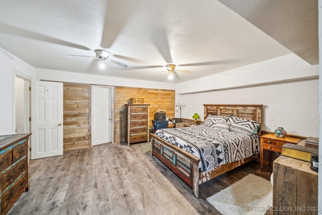 bedroom with wood walls, a textured ceiling, a ceiling fan, and wood finished floors