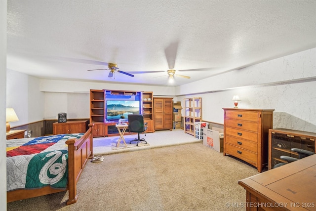 bedroom featuring carpet, a textured wall, wainscoting, ceiling fan, and a textured ceiling