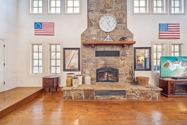 living area featuring a high ceiling, a fireplace, hardwood / wood-style flooring, and baseboards