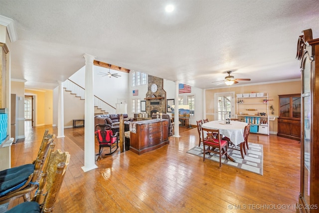 dining room with light wood-style floors, a fireplace, ceiling fan, and stairs