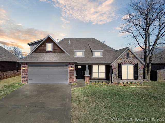 view of front of property featuring driveway, a lawn, stone siding, roof with shingles, and an attached garage