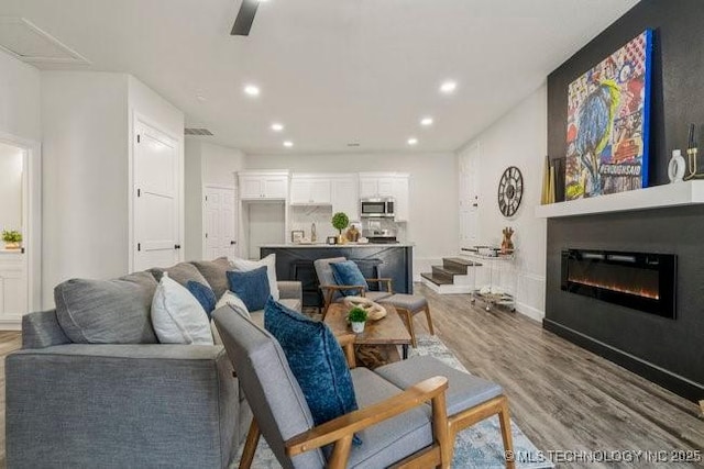 living area with a glass covered fireplace, ceiling fan, recessed lighting, and wood finished floors