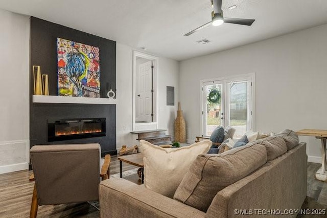 living room featuring visible vents, a ceiling fan, a glass covered fireplace, wood finished floors, and baseboards