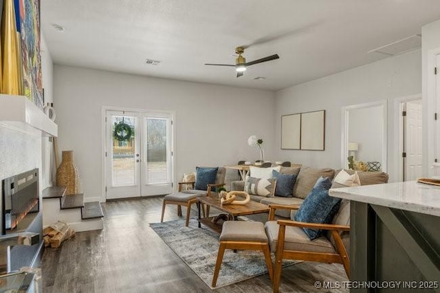 living room featuring a lit fireplace, a ceiling fan, wood finished floors, and french doors