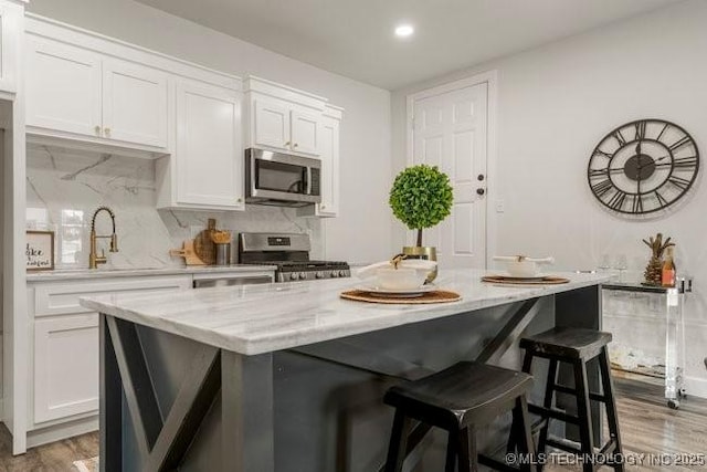 kitchen featuring light stone counters, white cabinetry, appliances with stainless steel finishes, backsplash, and a center island