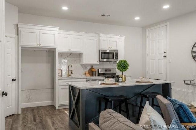 kitchen with stainless steel appliances, visible vents, white cabinetry, a sink, and a kitchen bar