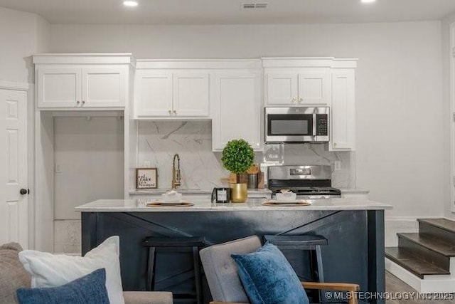 kitchen featuring an island with sink, white cabinetry, appliances with stainless steel finishes, and a breakfast bar area