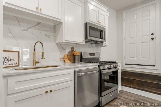 kitchen featuring decorative backsplash, appliances with stainless steel finishes, white cabinetry, a sink, and wood finished floors