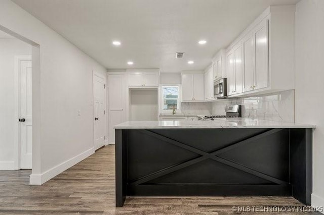 kitchen with appliances with stainless steel finishes, backsplash, white cabinetry, and a peninsula