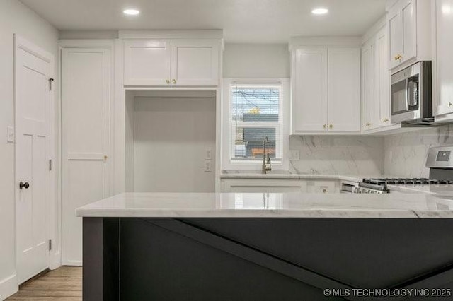 kitchen with stainless steel microwave, backsplash, range, and white cabinetry