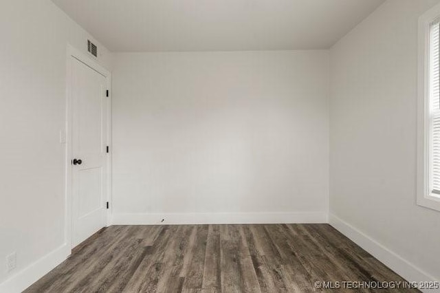 spare room featuring a wealth of natural light, visible vents, baseboards, and dark wood-type flooring