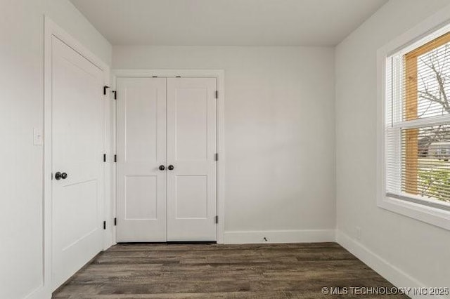 unfurnished bedroom with a closet, dark wood finished floors, and baseboards