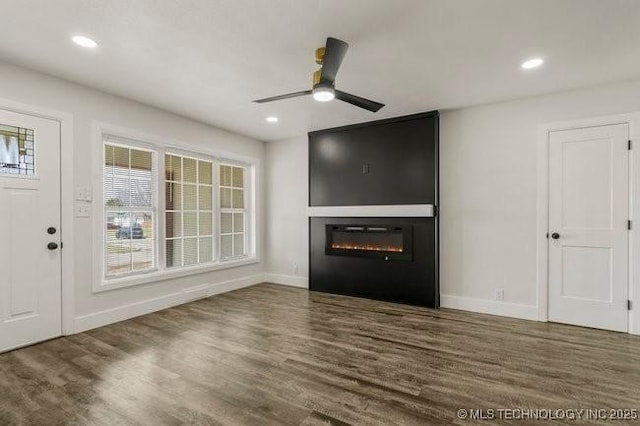 unfurnished living room with wood finished floors, recessed lighting, a glass covered fireplace, and baseboards