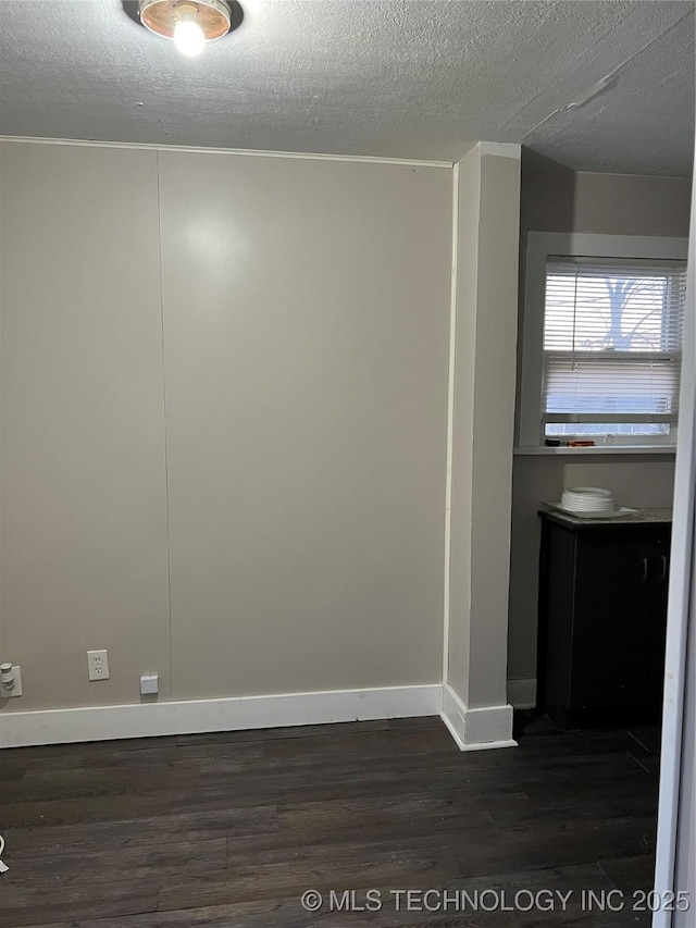 spare room with dark wood-type flooring, a textured ceiling, and baseboards