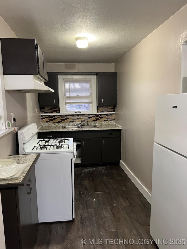 kitchen featuring dark cabinets, white appliances, dark wood-type flooring, a sink, and tasteful backsplash