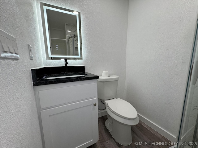 bathroom with baseboards, a textured wall, toilet, wood finished floors, and vanity