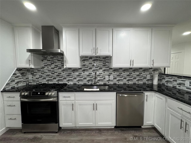 kitchen with appliances with stainless steel finishes, white cabinets, a sink, and wall chimney range hood