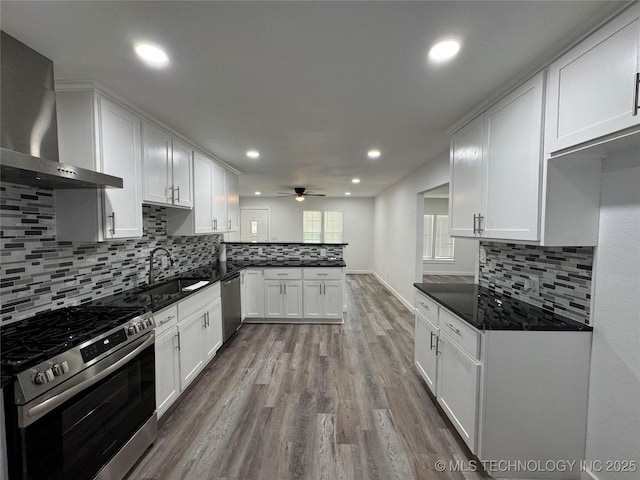 kitchen featuring stainless steel appliances, a peninsula, a sink, white cabinets, and wall chimney range hood