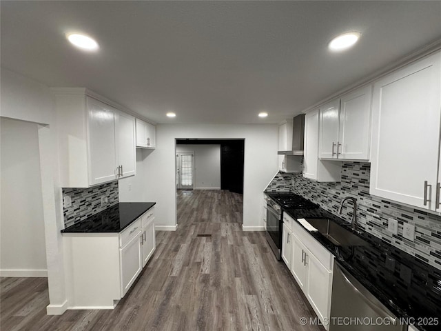 kitchen with dark countertops, appliances with stainless steel finishes, wall chimney range hood, white cabinetry, and a sink