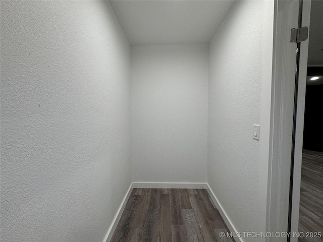 hall featuring dark wood-style floors, baseboards, and a textured wall