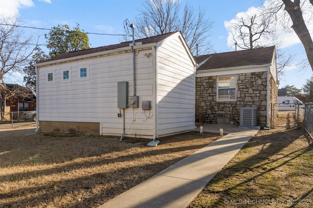 view of home's exterior featuring fence, stone siding, central AC, and a shingled roof