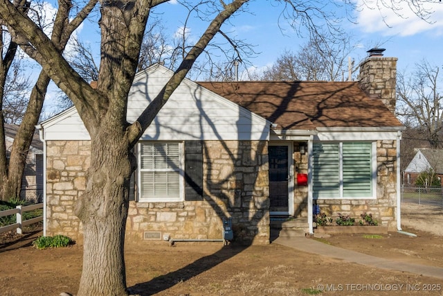 view of front of home featuring stone siding, a chimney, and fence