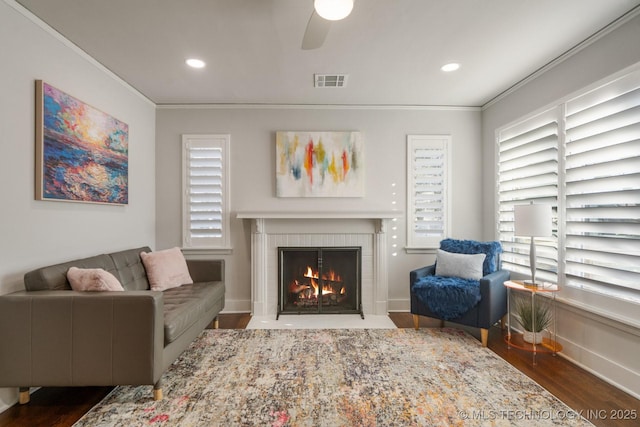 living room with visible vents, crown molding, a fireplace, wood finished floors, and a ceiling fan