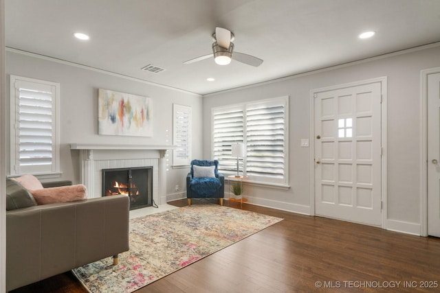 living room with visible vents, crown molding, a fireplace, wood finished floors, and a ceiling fan