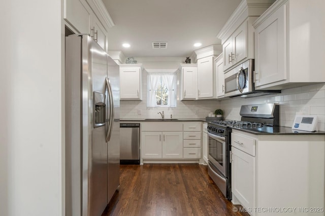 kitchen with visible vents, a sink, stainless steel appliances, white cabinetry, and dark countertops