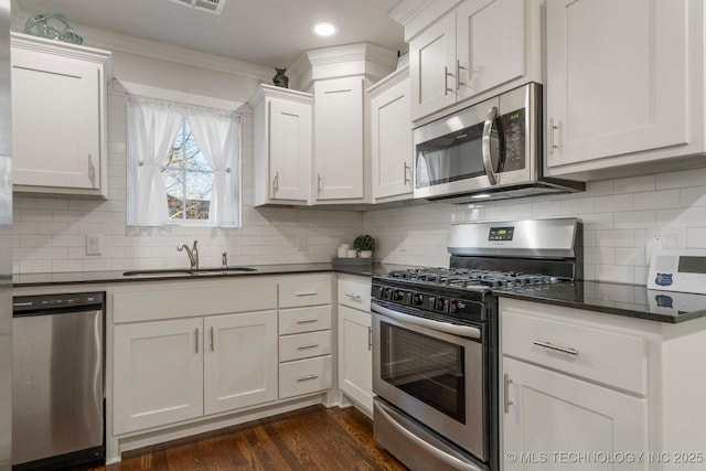 kitchen with dark countertops, stainless steel appliances, dark wood-style floors, white cabinetry, and a sink