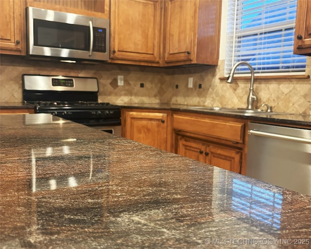 kitchen featuring appliances with stainless steel finishes, dark stone counters, a sink, and tasteful backsplash