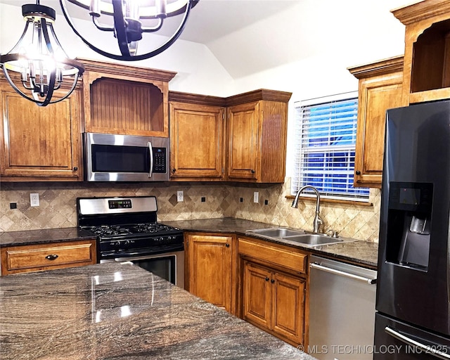 kitchen with brown cabinetry, lofted ceiling, appliances with stainless steel finishes, a chandelier, and a sink